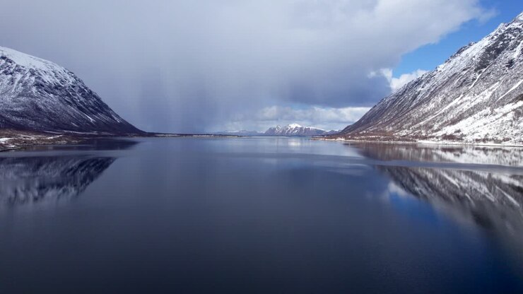 Ripresa aerea in avanti del Morfjorden a Lofoten durante l'inverno con una tempesta di neve, giornata parzialmente nuvolosa