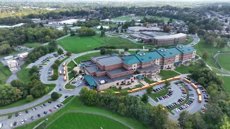 High-aerial-view-of-large-American-high-school-with-line-of-yellow-school-buses-during-dismissal