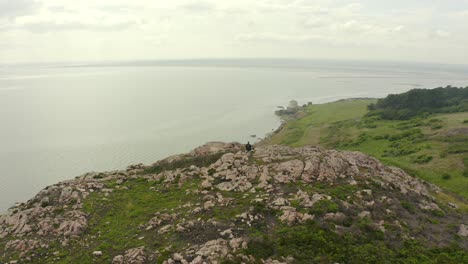 Aerial-panning-shot,-Man-sitting-down-with-his-dog-on-to-top-of-hill-enjoying-the-view