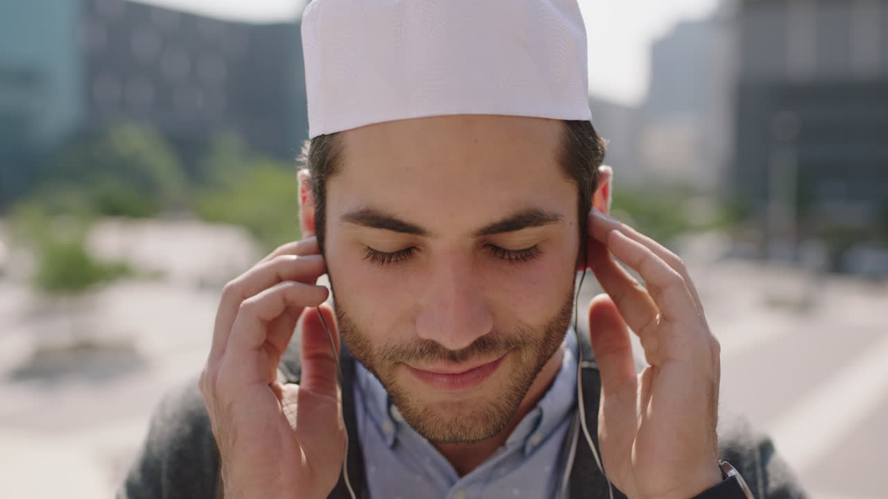 retrato de un atractivo joven musulmán de oriente medio sonriendo alegremente disfrutando de la música con auriculares en el fondo de la ciudad urbana