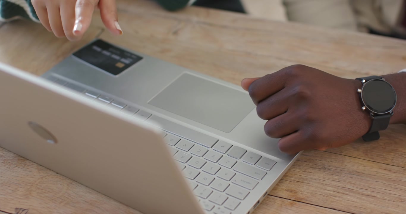 African American colleagues working on silver laptop on table, man entering, woman tapping sticker