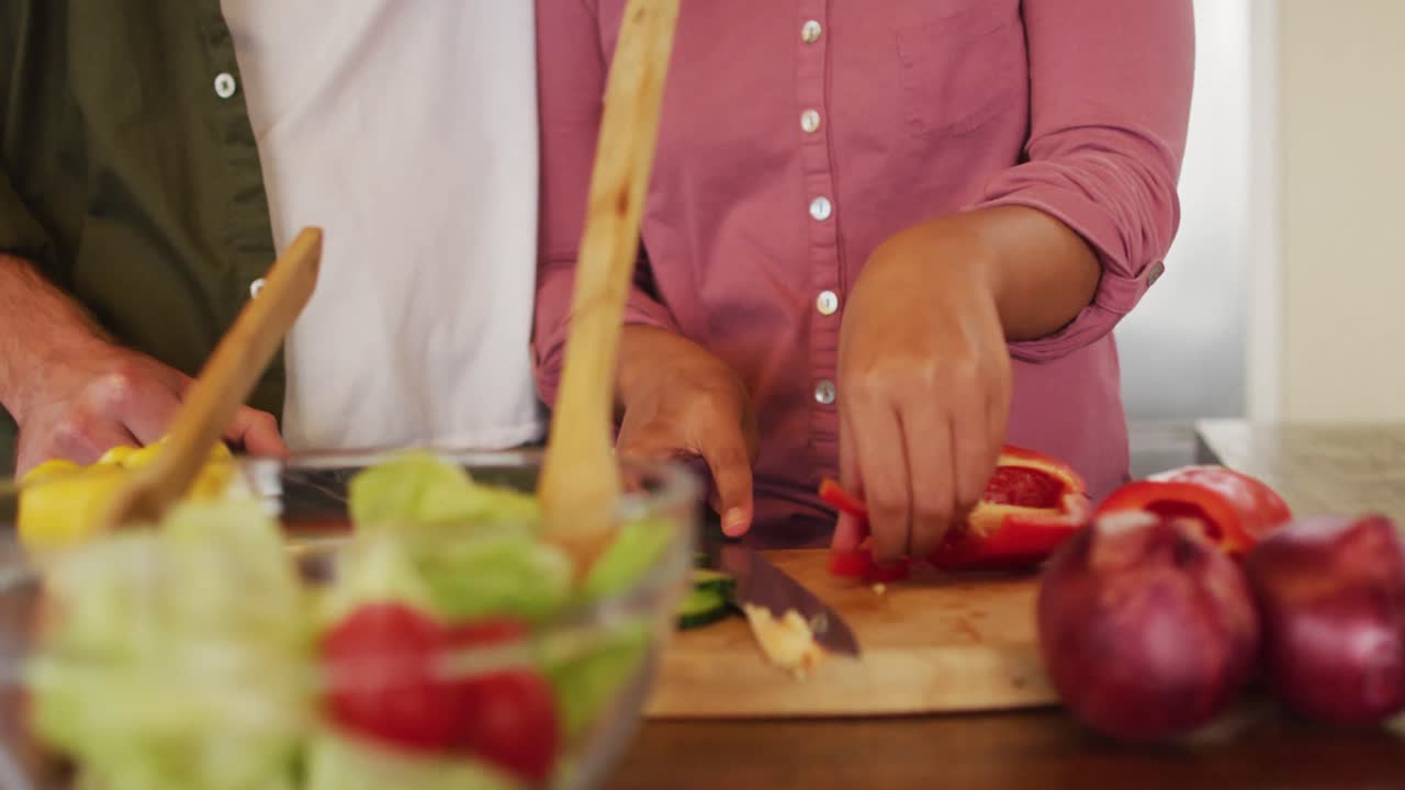sección media de una pareja diversa preparando comida juntos en la cocina, cortando verduras para ensalada