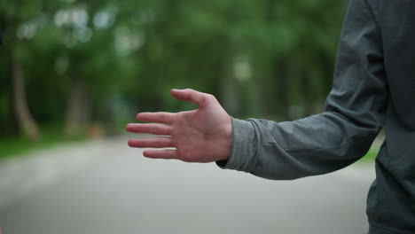 close-up of two hands interacting playfully with a knuckle bump, one hand, in a grey sleeve, reaches out towards another, against a blurred park background featuring greenery and buildings