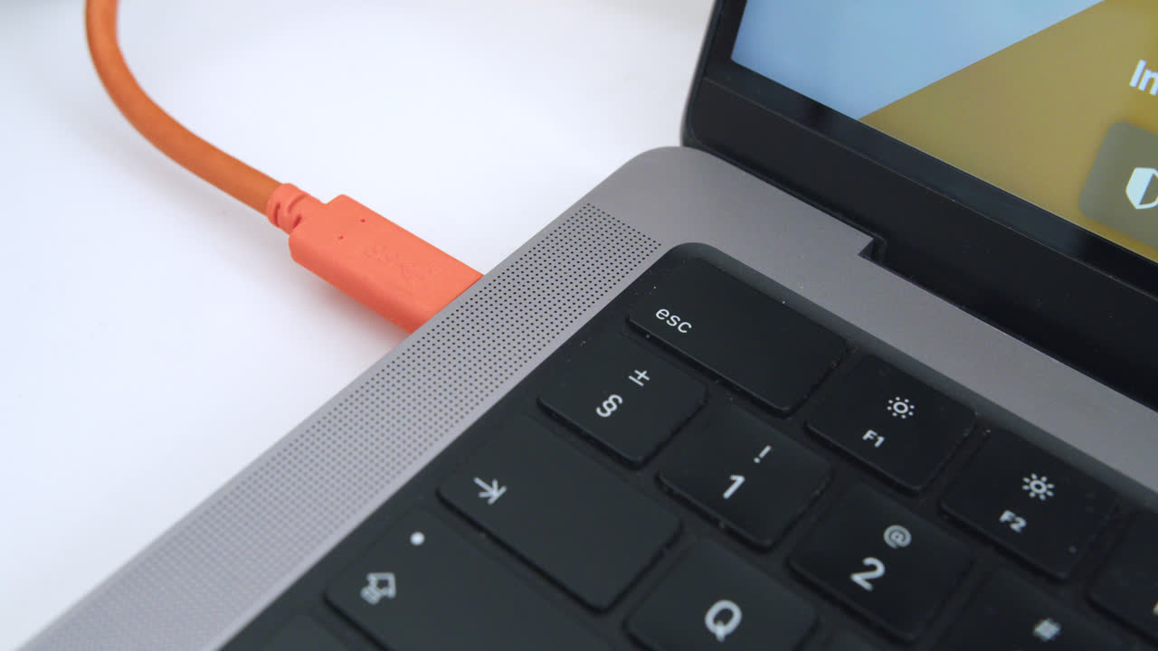 increíble cámara lenta de primer plano toma de la mano del joven conectando el cable usb c de disco de encaje naranja en el ordenador macbook pro en la oficina con luz natural y mesa blanca