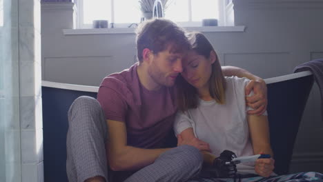 disappointed couple with woman with prosthetic arm sitting in bathroom with negative pregnancy test