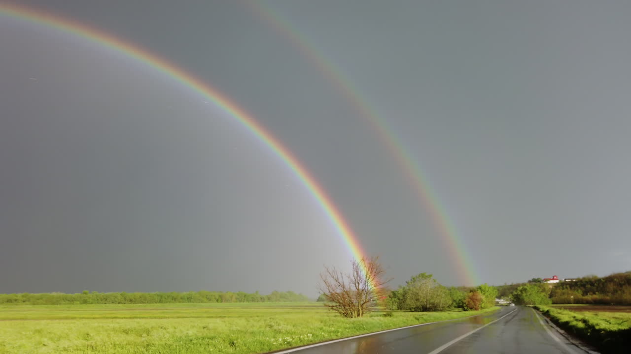 Rainy road with a double rainbow on the horizon