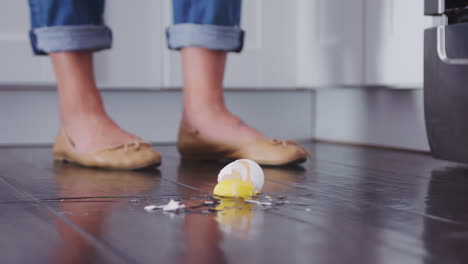 un huevo cayendo al suelo de la cocina y rompiéndose en las tablas del suelo de madera, ángulo bajo, movimiento lento