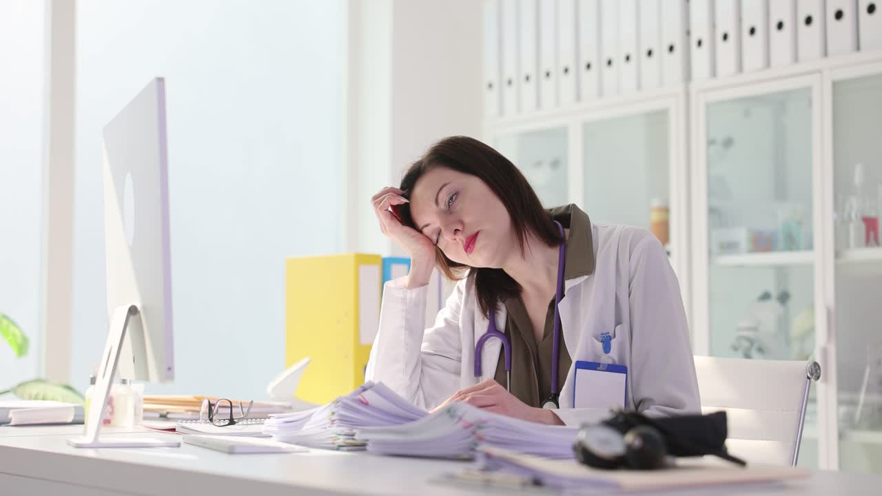 Tired female doctor overwhelmed with paperwork in office