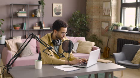 man wearing glasses and sitting at a table with microphone while typewriting on laptop