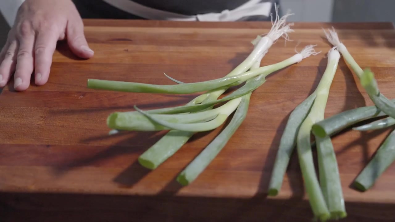 Een statisch shot van een chef-kok die het beeld binnenkomt en een lente-ui op een snijplank gooit, wat de opwinding van voedselbereiding toont. Ideaal voor culinaire en kookinhoud in een professionele keuken