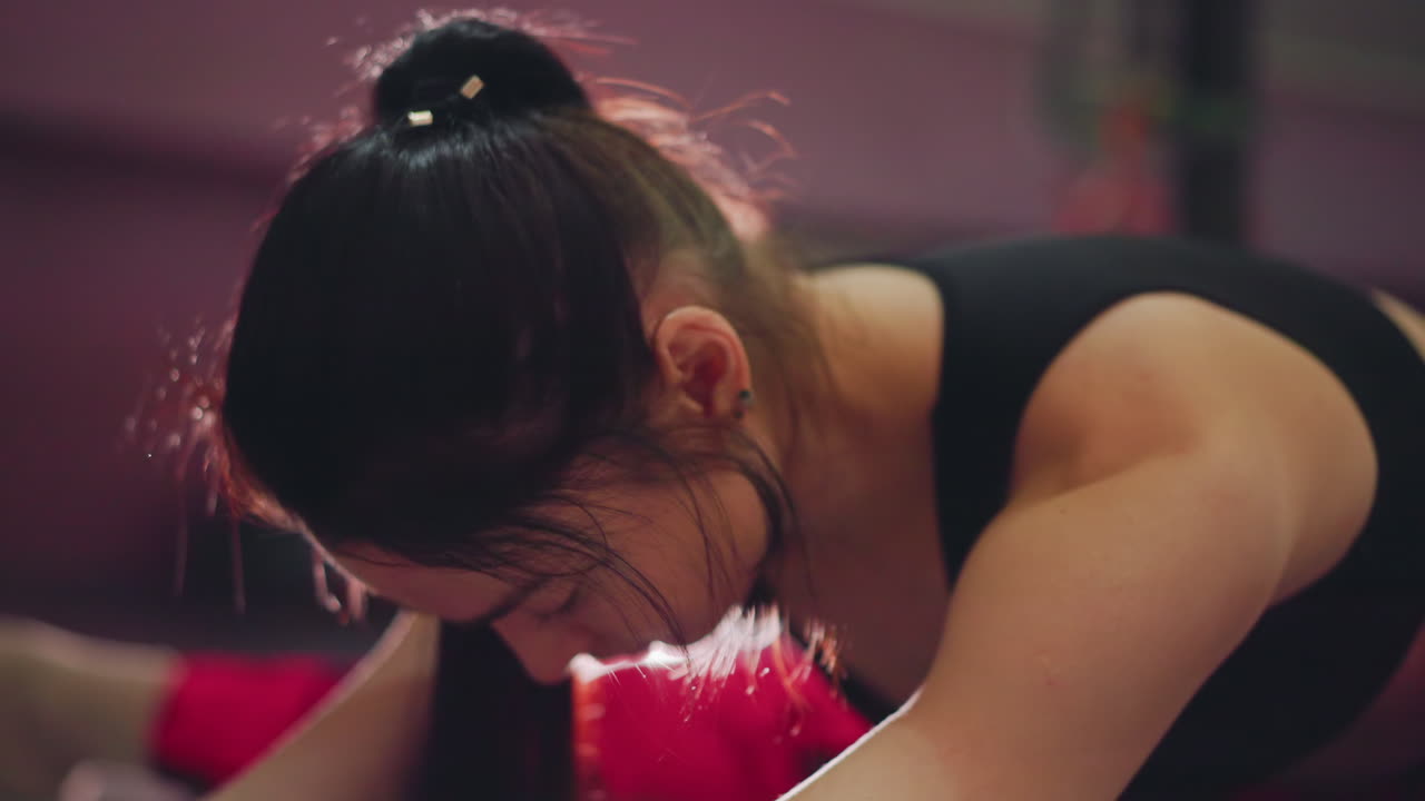 Donna asiatica in primo piano concentrata sul respiro e sul movimento, ritratto di riscaldamento in studio con bagliore in controluce, sudore sulla pelle, coda di cavallo legata, visibile forza delle spalle, intensa concentrazione, pratica di respirazione.