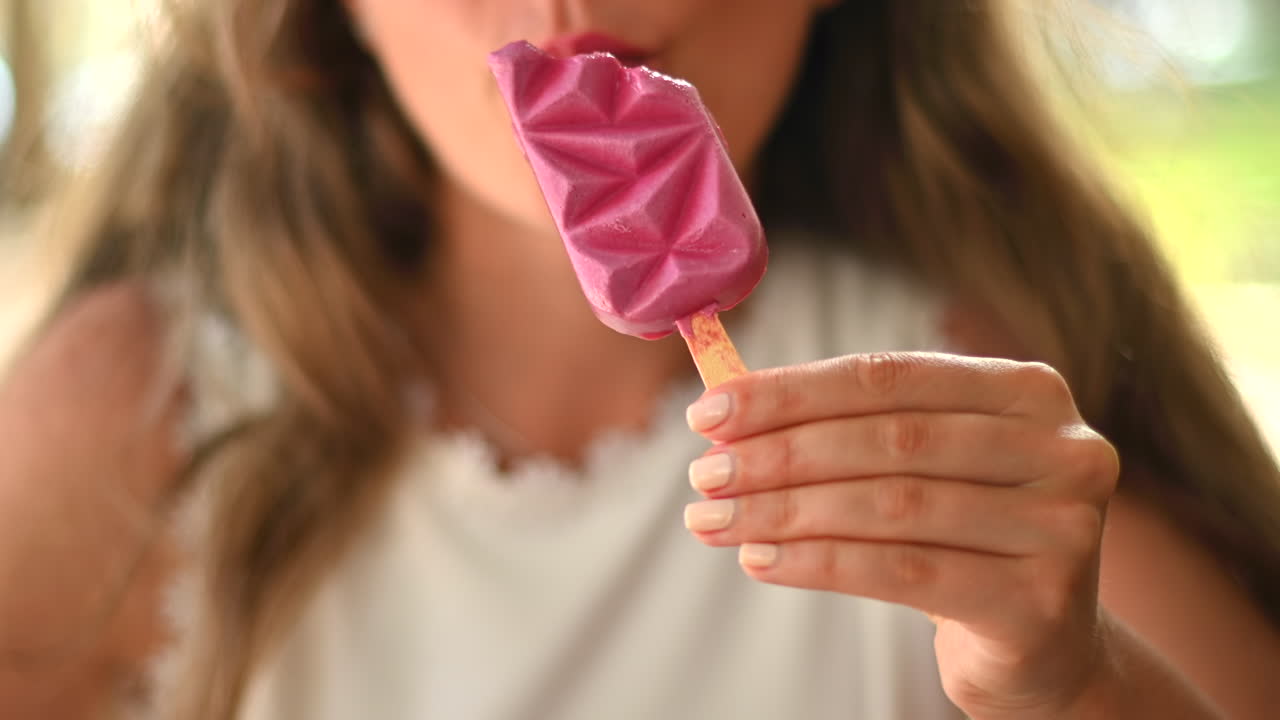 Donna bruna che mangia un gelato rosa in un bar, alla luce del giorno