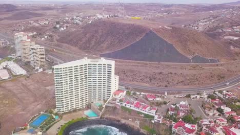View-from-a-drone-ascending-over-the-sea-showing-a-hotel-zone-next-to-the-coast-with-a-highway-behind-it-in-Mexico