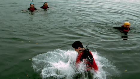 man in wet suit doing a somersault into a lake