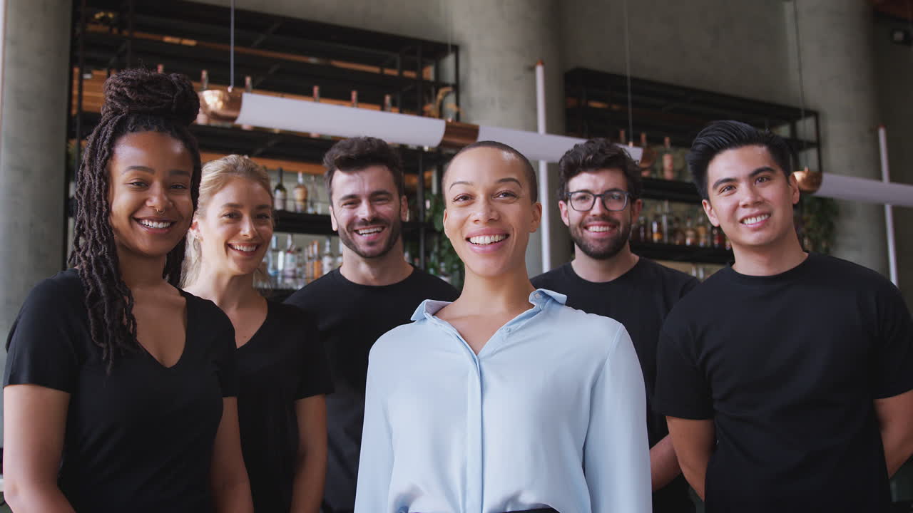 retrato de una mujer sonriente dueña de un bar de restaurantes con un equipo de personal de espera de pie en el mostrador