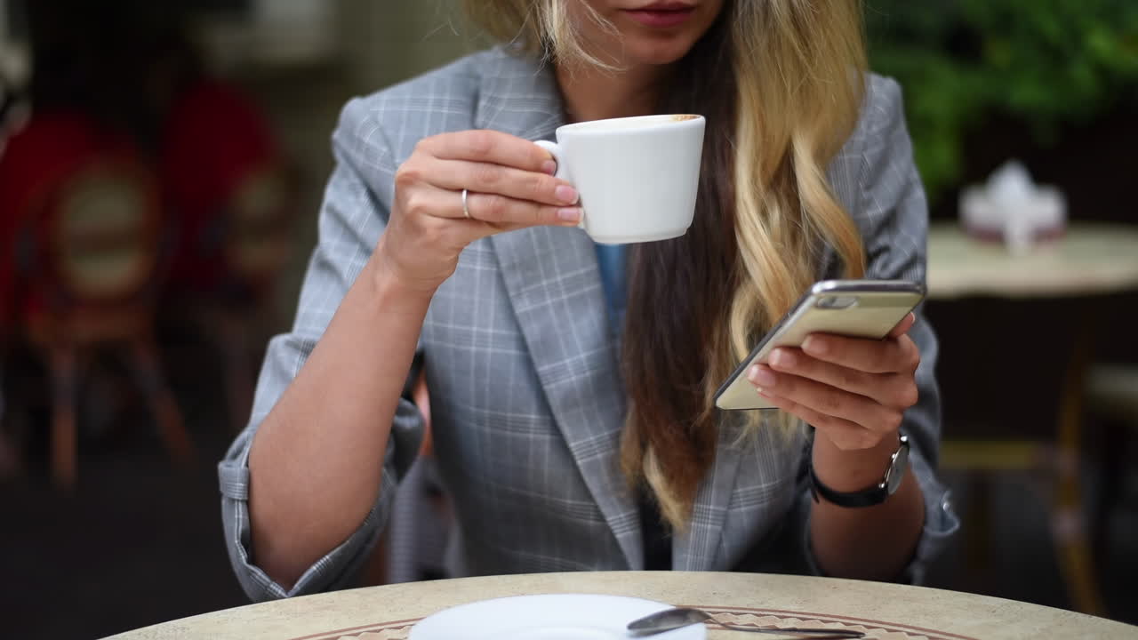 Primo piano di una donna che scrive un messaggio sul suo telefono mentre beve un caffè su una terrazza