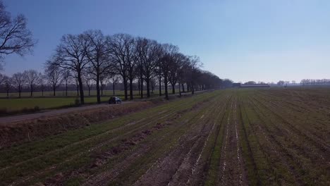 Drone-shot-of-a-car-driving-on-a-road-between-meadows-farmland