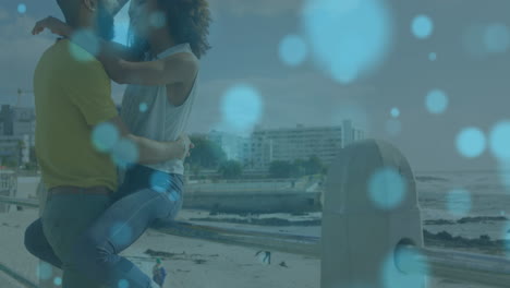 Animation-of-light-spots-over-african-american-couple-embracing-at-beach