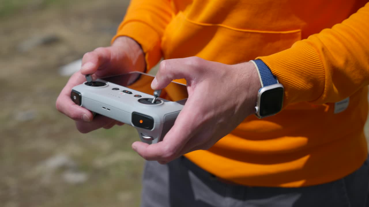 piloto de avión no tripulado con chaqueta naranja usando el controlador de avión no tripulado dji, ángulo alto