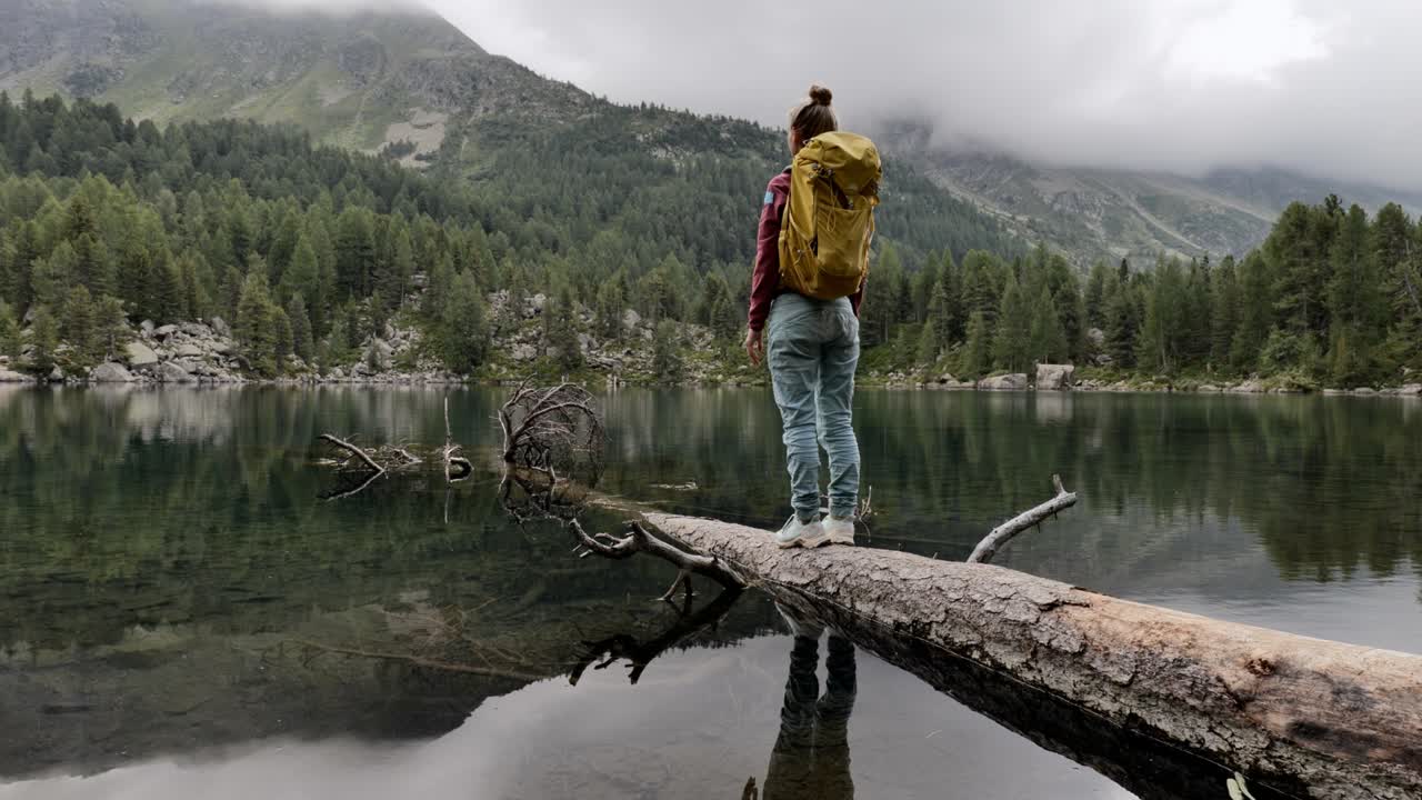 Young woman walks on tree trunk above alpine lake