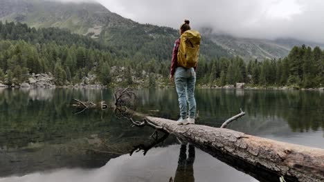 young woman walks on tree trunk above alpine lake