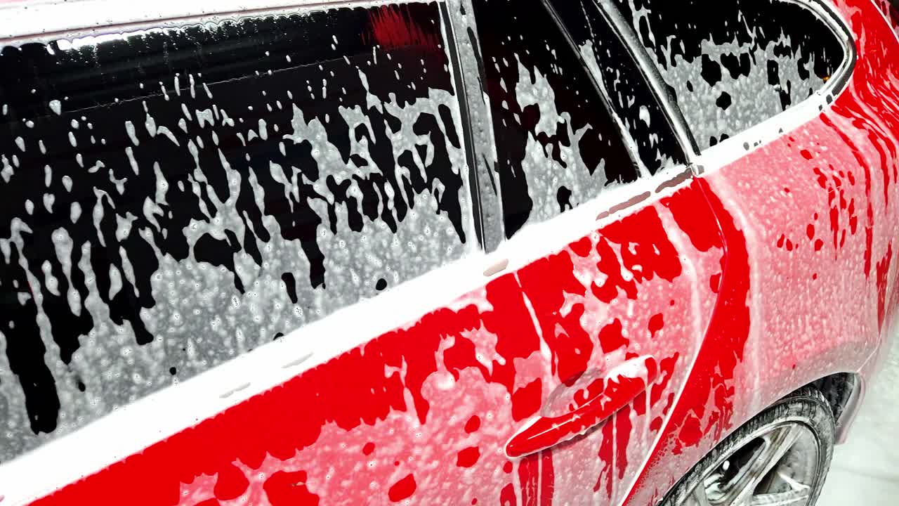 Primo piano del finestrino di un'auto rossa coperto di schiuma durante il lavaggio, che crea un aspetto fresco.