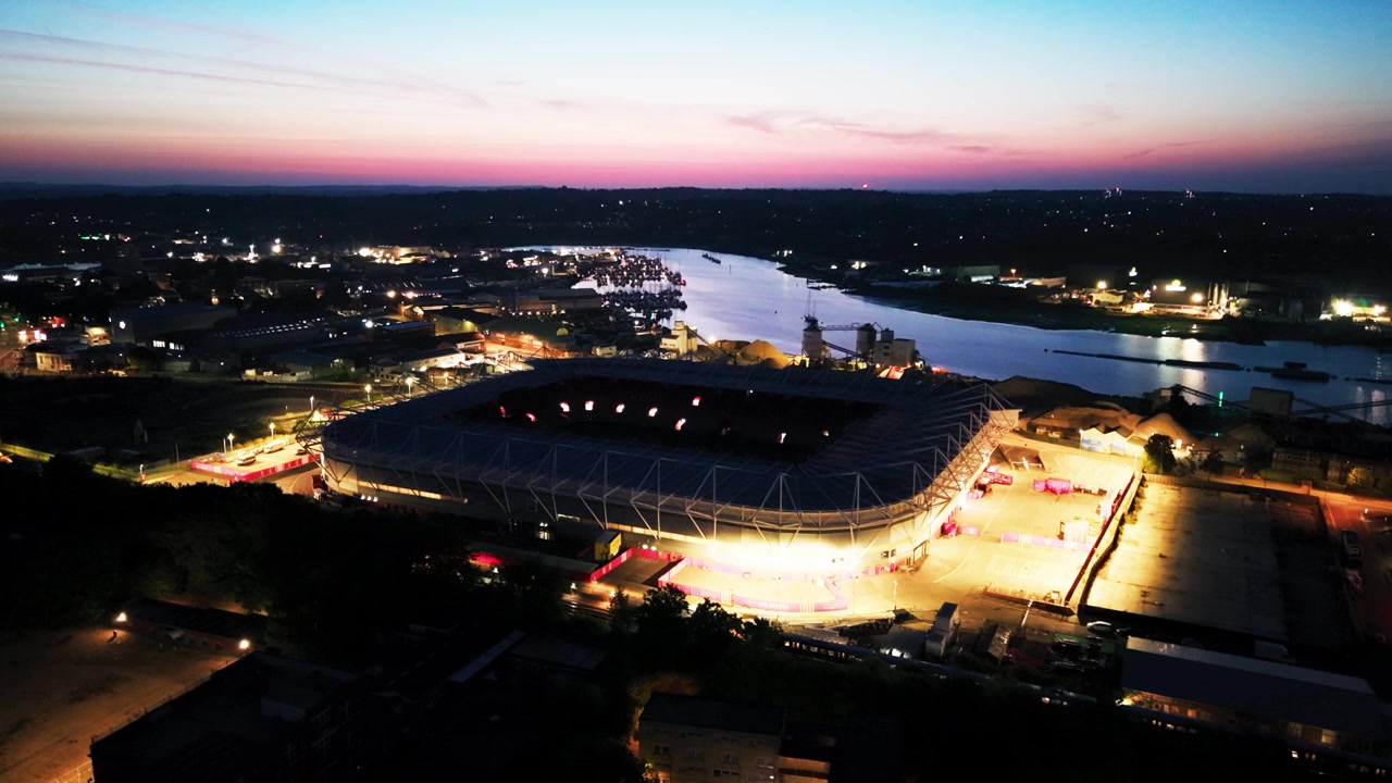 Droneutsikt over St Marys Stadium som gløder under en blå og rosa himmel før daggry, med bylys og elven Itchen bortenfor