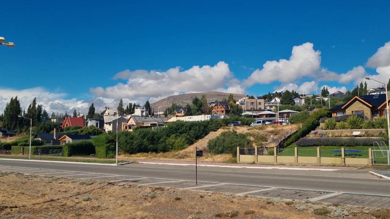 Scena residenziale tranquilla a El Calafate, Argentina, con piccole case, nuvole alla deriva e una strada vuota in una giornata di sole, che cattura il ritmo calmo della vita quotidiana in Patagonia.