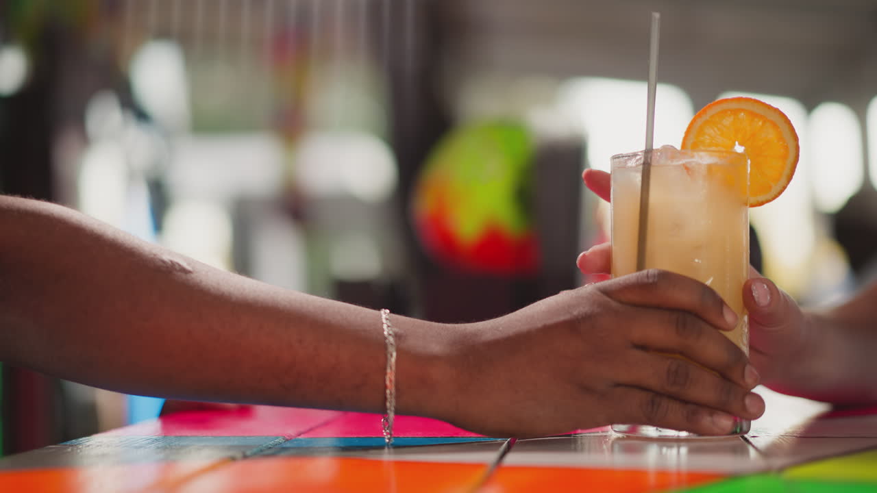 el camarero sirve un cóctel para el invitado en un bar de primer plano. un hombre afroamericano empuja un vaso con una bebida exótica a una joven turista. el camarero serve una bebida