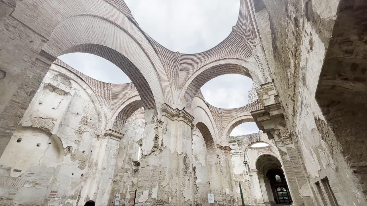 Interior of ancient cathedral ruins in Guatemala, featuring stunning brick arches and weathered walls against a cloudy sky.