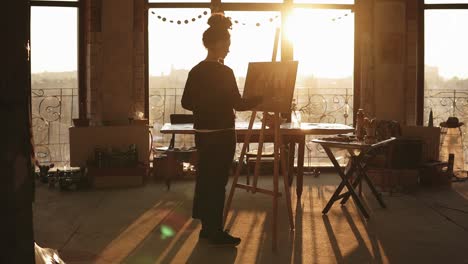 fully concentrated sophisticated female artist in her 20's is drawing picture on easelin a minimalistic loft styled art studio.