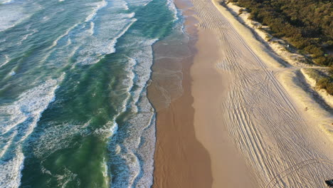 Aerial-view-passing-a-car-on-the-K'gari-beach,-sunny-morning-on-Fraser-island-in-Australia