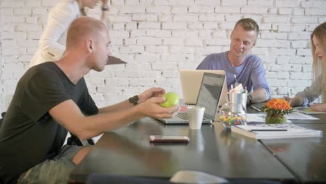 los colegas de negocios están sentados en la mesa y explican algo al empleado en la computadora portátil. los compañeros de trabajo discuten en equipo el proyecto de negocio usando la computadora portable. una mujer está escribiendo algo en un cuaderno