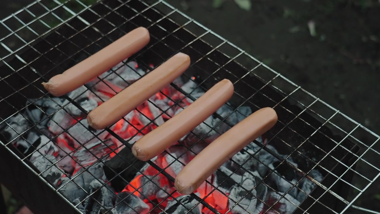 Mano che posiziona salsicce crude su una griglia calda per barbecue