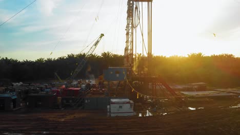 Cinematic-4K-Drone-Footage-of-Onshore-Drilling-Rig-equipment-structure-for-oil-exploration-and-exploitation-in-the-middle-of-jungle-surrounded-by-palm-oil-trees-during-sunset-and-high-oil-price