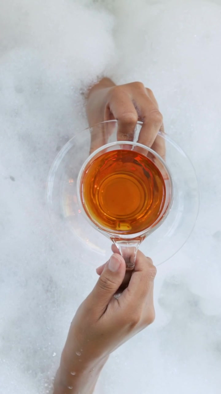 Video verticale: Una donna che emerge dalla schiuma posa una tazza su un piattino nella vasca da bagno, portando la tazza per sorseggiare.
