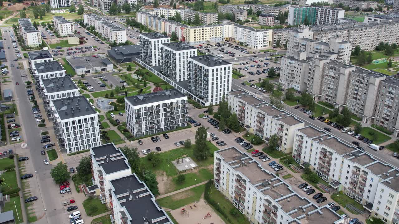 Aerial view of a dense residential district showing a mix of older mid-rise blocks and newer apartment buildings, arranged around courtyards, parking areas, and tree-lined pathways