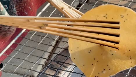 close-up of a rice cracker being flipped on a grill using bamboo tongs over open flames.