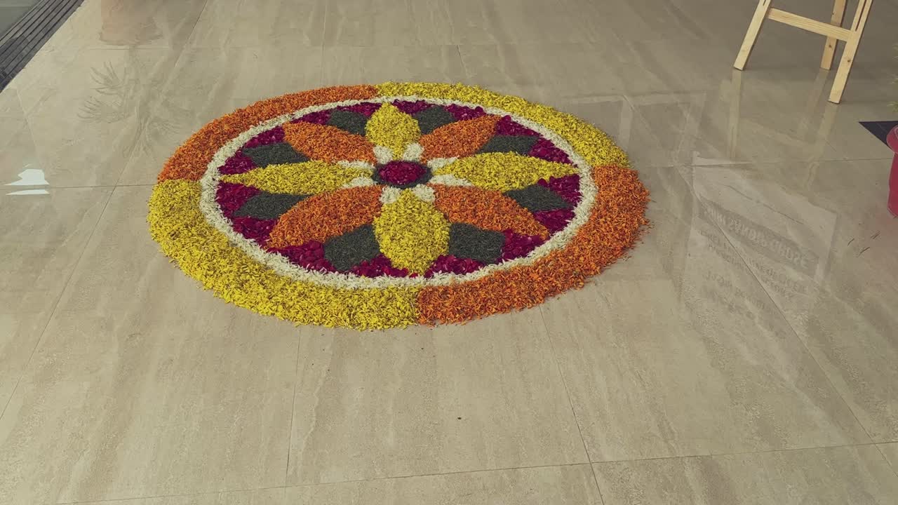 Vibrant circular rangoli created with colorful flower petals arranged in a symmetrical pattern on a smooth floor, designed to warmly welcome arriving guests