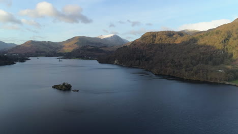 high aerial drone shot over ullswater lake with snowy helvellyn mountain on sunny and cloudy morning lake district cumbria united kingdom