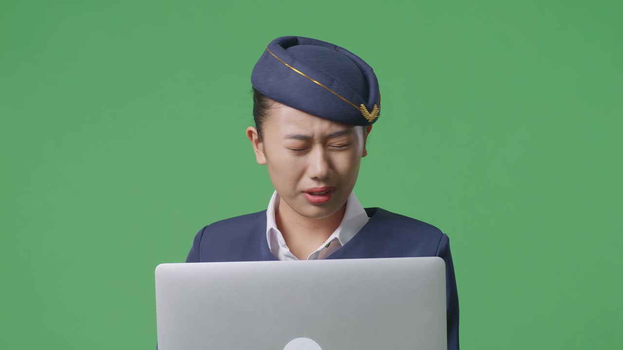 녹색 스크린 배경 스튜디오에 서 있는 동안 노트북을 사용하고 두통을 고 있는 아시아 여성 승무원의 클로즈업