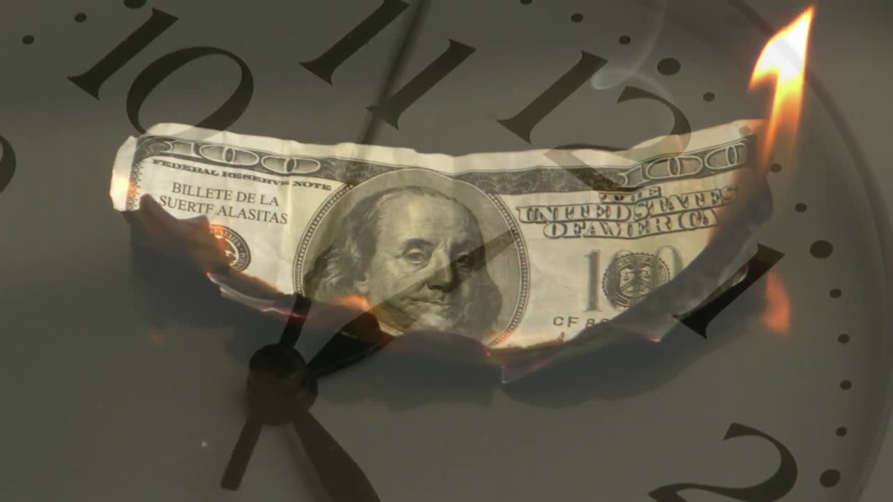 Animazione di una banconota di dollaro americano che brucia, con un orologio che si muove velocemente sullo sfondo