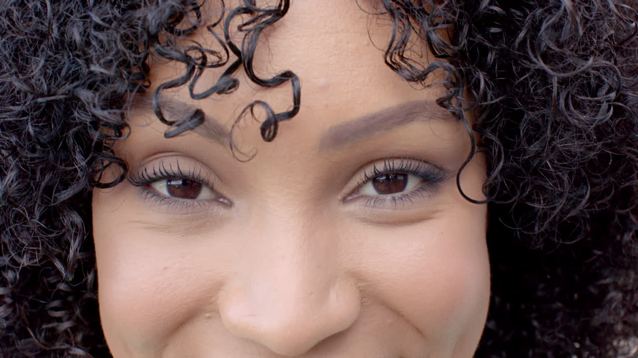 Close-up of woman with curly hair smiling and looking at camera