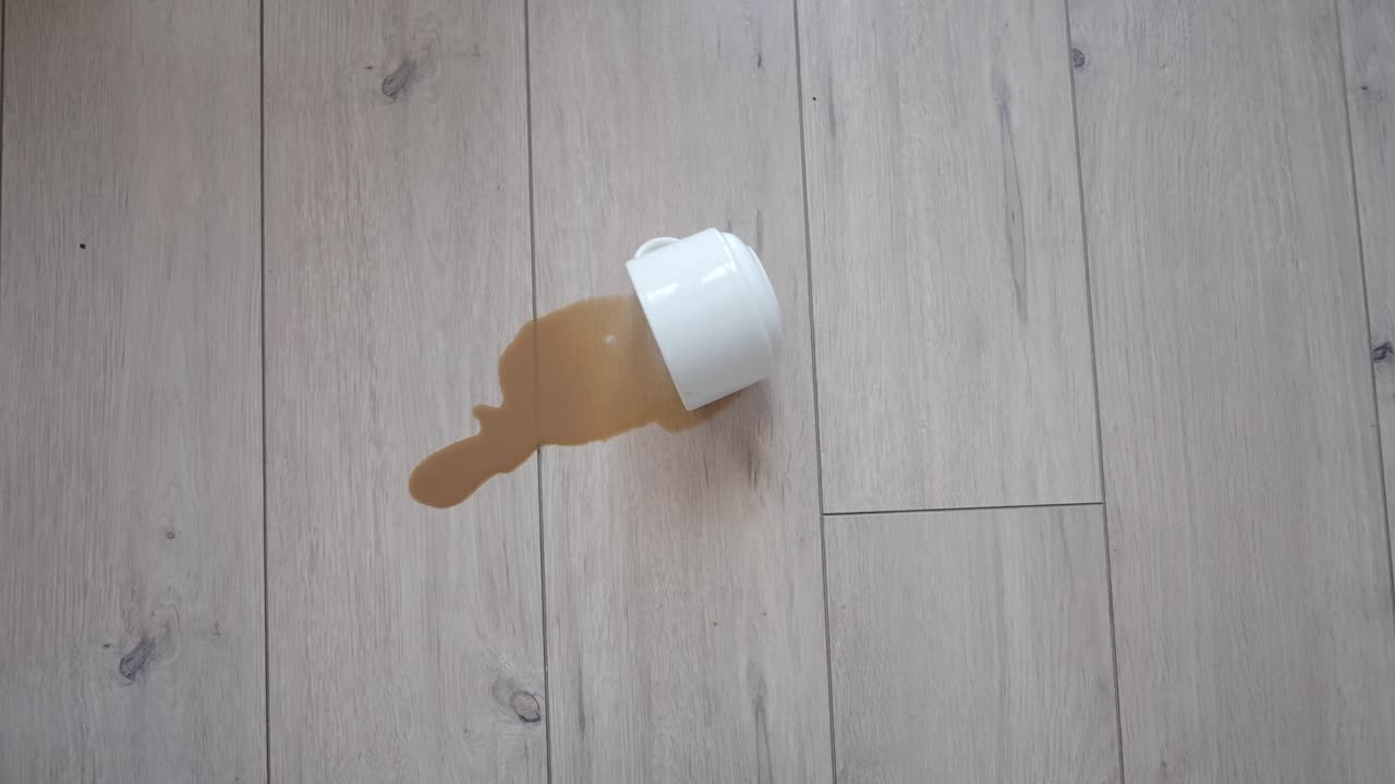 Hvitt krus søler kaffe på et tregulv.