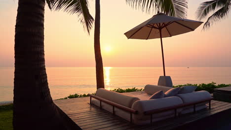 seaside lounge with bed and beach umbrella silhouette on the picturesque orange sunset over the sea