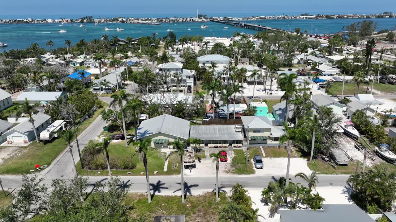 Luxury residential area of american town in Florida with palm trees and blue river water in background. Aerial wide shot. Cruising boats on clear bay with bridge in distance.