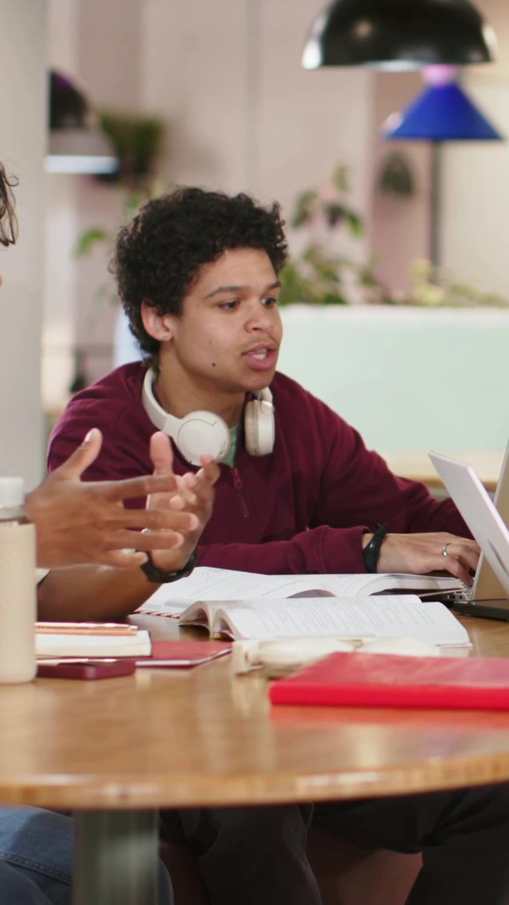 Vertical video: Reacting to peer tablet, student typing on laptop in lounge, maroon top, headphones