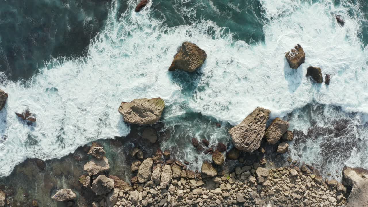 Vista aerea dall'alto delle onde dell'oceano che si infrangono su una costa rocciosa dorata.