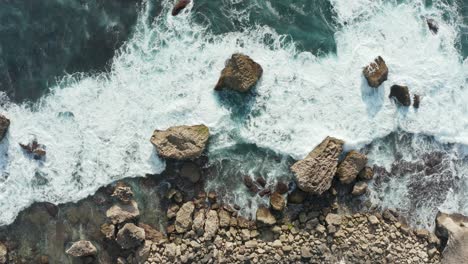 aerial top down view of ocean waves crashing into golden rocky shore