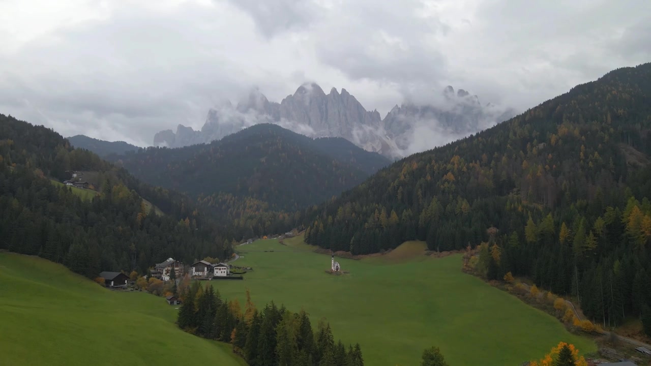 Et luftfoto af Sankt Maddalena kirke beliggende i Val di Funes, omgivet af den majestætiske Odle-bjerggruppe på en overskyet efterårsdag, afslører et malerisk landskab i Sydtyrol, Italien.